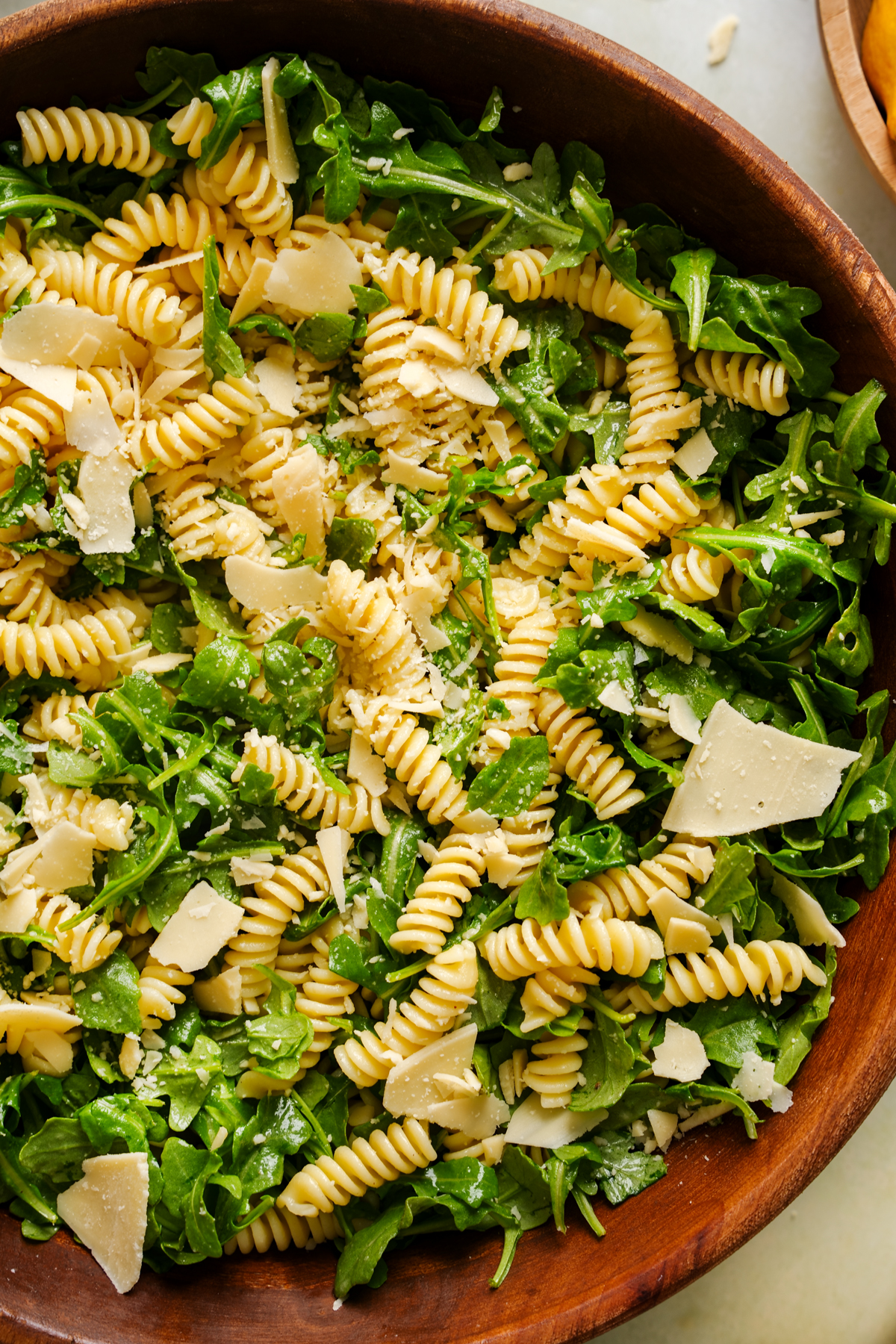 Close-up of a fresh lemon arugula pasta salad in a wooden bowl, featuring rotini pasta, organic arugula, and shaved vegan parmesan tossed in a light lemon vinaigrette.