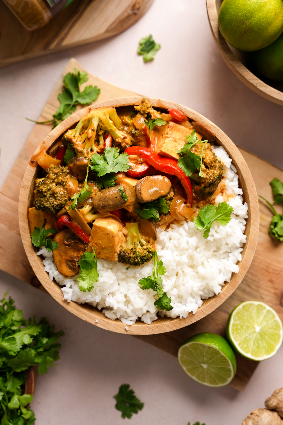 Nut-free vegan Panang curry with tofu, broccoli, mushrooms, and red bell peppers in a creamy sunflower seed butter sauce, served over fluffy white rice and garnished with fresh cilantro, surrounded by lime wedges, cilantro leaves, and fresh ingredients.