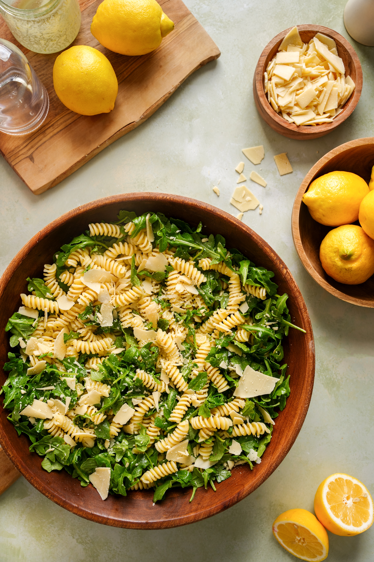 Bright and refreshing lemon arugula pasta salad featuring spiral pasta, fresh arugula, and vegan parmesan shavings in a large wooden bowl, perfect for a healthy plant-based lunch or side dish.