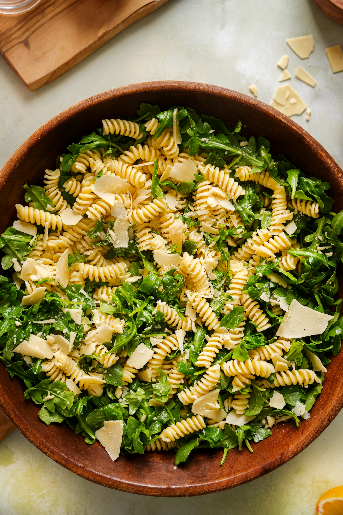 Overhead view of a vibrant vegan lemon arugula pasta salad in a wooden bowl, made with rotini pasta, fresh baby arugula, and shaved vegan parmesan, tossed in a light lemon dressing.