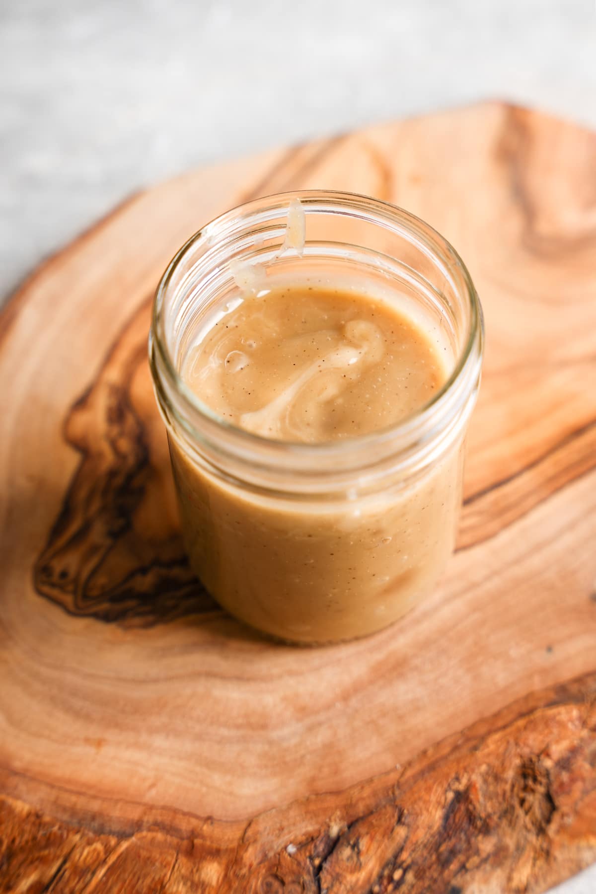 A glass jar filled with smooth, creamy dairy-free sweetened condensed milk placed on a rustic wooden board. The mixture has a glossy, caramel-colored texture with visible vanilla specks, showcasing its rich and homemade quality.