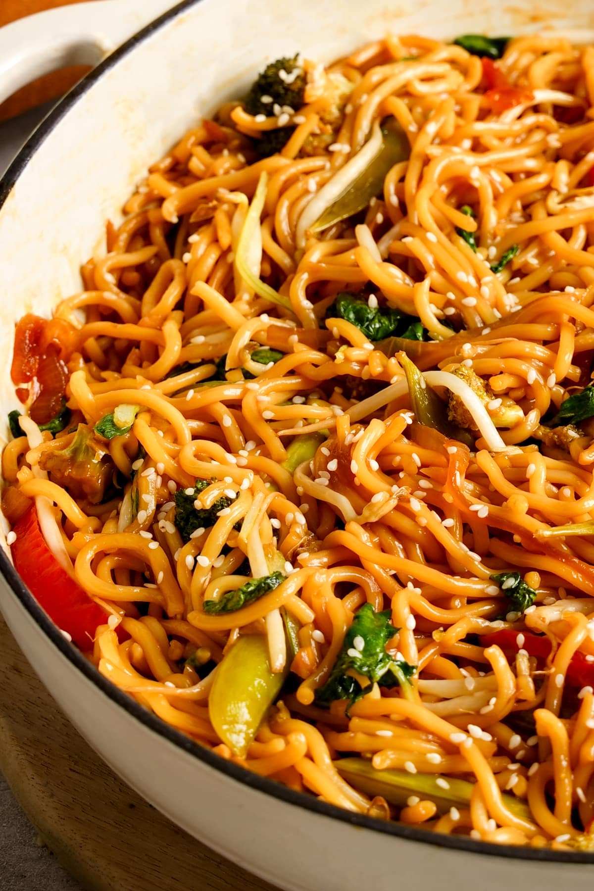 A pot of plant-based chow mein noodles tossed with vegetables including bell peppers, broccoli, and bok choy, coated in a glossy soy-based sauce. The dish is garnished with sesame seeds, creating a colorful and flavorful vegan stir-fry presentation.