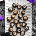 Vegan SunButter chocolate eyeballs arranged on a white scalloped platter, each coated in dark chocolate with candy eyes on top for a fun Halloween treat, surrounded by black lace and colorful flowers.