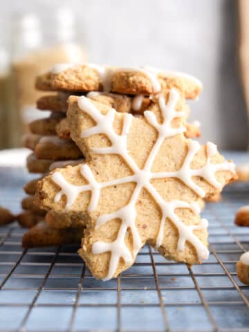 Stack of almond-flour snowflake sugar cookies on a cooling rack, decorated with white vanilla icing in intricate snowflake patterns.