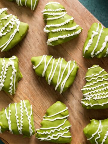 Assorted green chocolate Christmas tree treats decorated with white drizzle, arranged on a wooden serving board for a healthy holiday dessert.