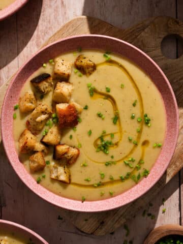Creamy vegan potato soup topped with crispy croutons, fresh chives, and a drizzle of olive oil in a rustic bowl