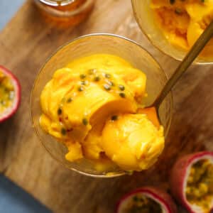 A close-up of creamy homemade passion fruit sorbet topped with fresh passion fruit pulp in a glass dessert bowl. This easy vegan passion fruit sorbet is naturally dairy-free, gluten-free, refined sugar-free, and bursting with bright tropical flavor.