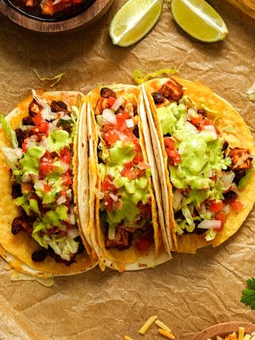 Overhead view of loaded vegan tofu tacos filled with seasoned tofu and black beans, shredded lettuce, pico de gallo, and creamy cilantro lime dressing, served with lime wedges and fresh cilantro.